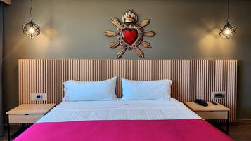A hotel room with a bed, two bedside tables, a wall-mounted decorative piece, and two hanging light fixtures.