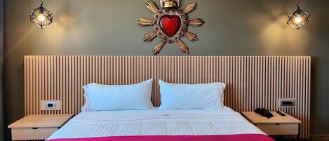 Quarto de hotel com cama, duas mesas de cabeceira, um objeto decorativo na parede e duas luminárias pendentes.
