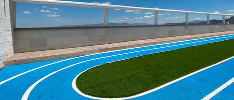 Pista de atletismo azul con marcas blancas de carriles, rodeada por un muro de concreto y una barandilla blanca.