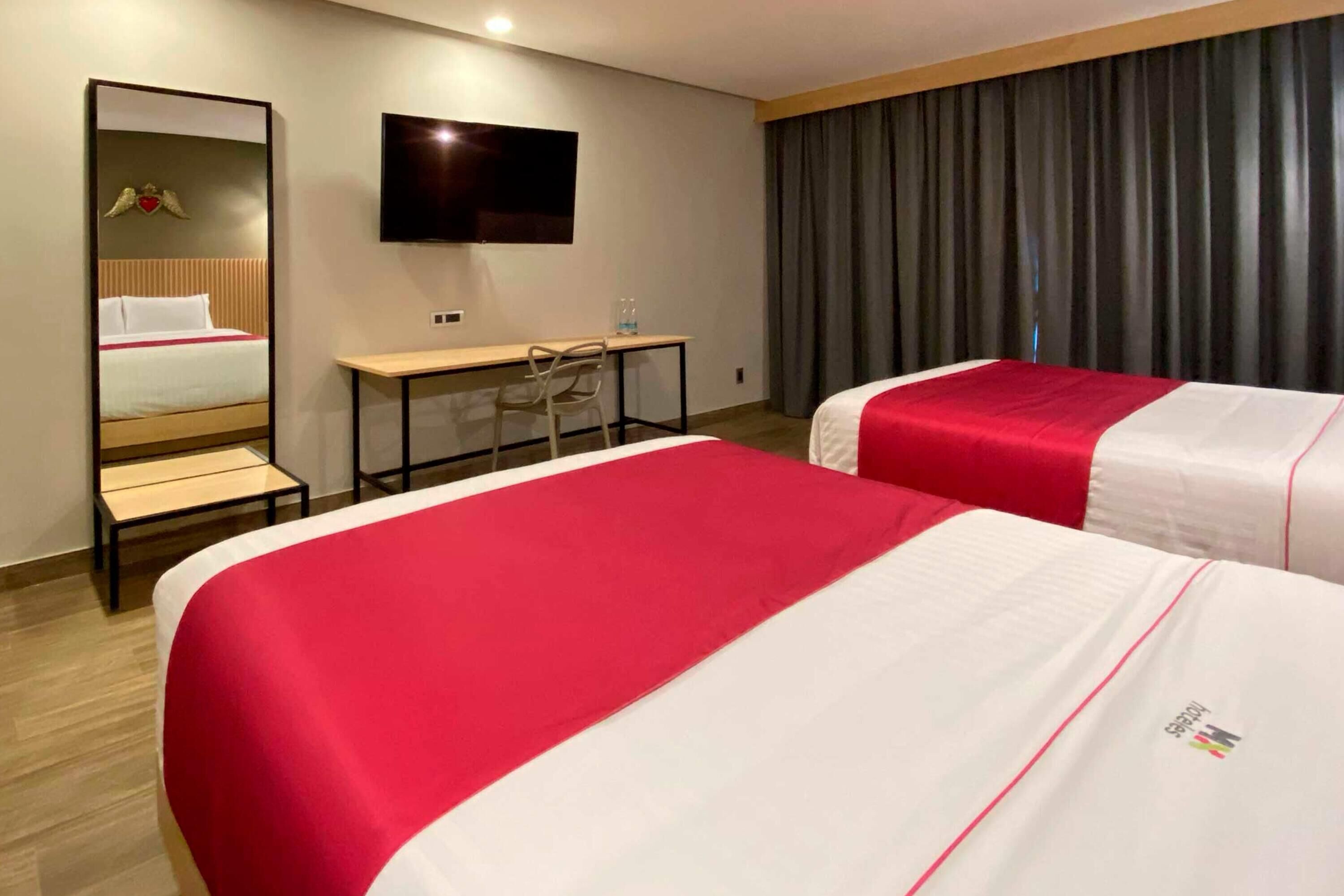 Camera d'albergo con due letti, una scrivania, una sedia, una televisione e uno specchio grande.