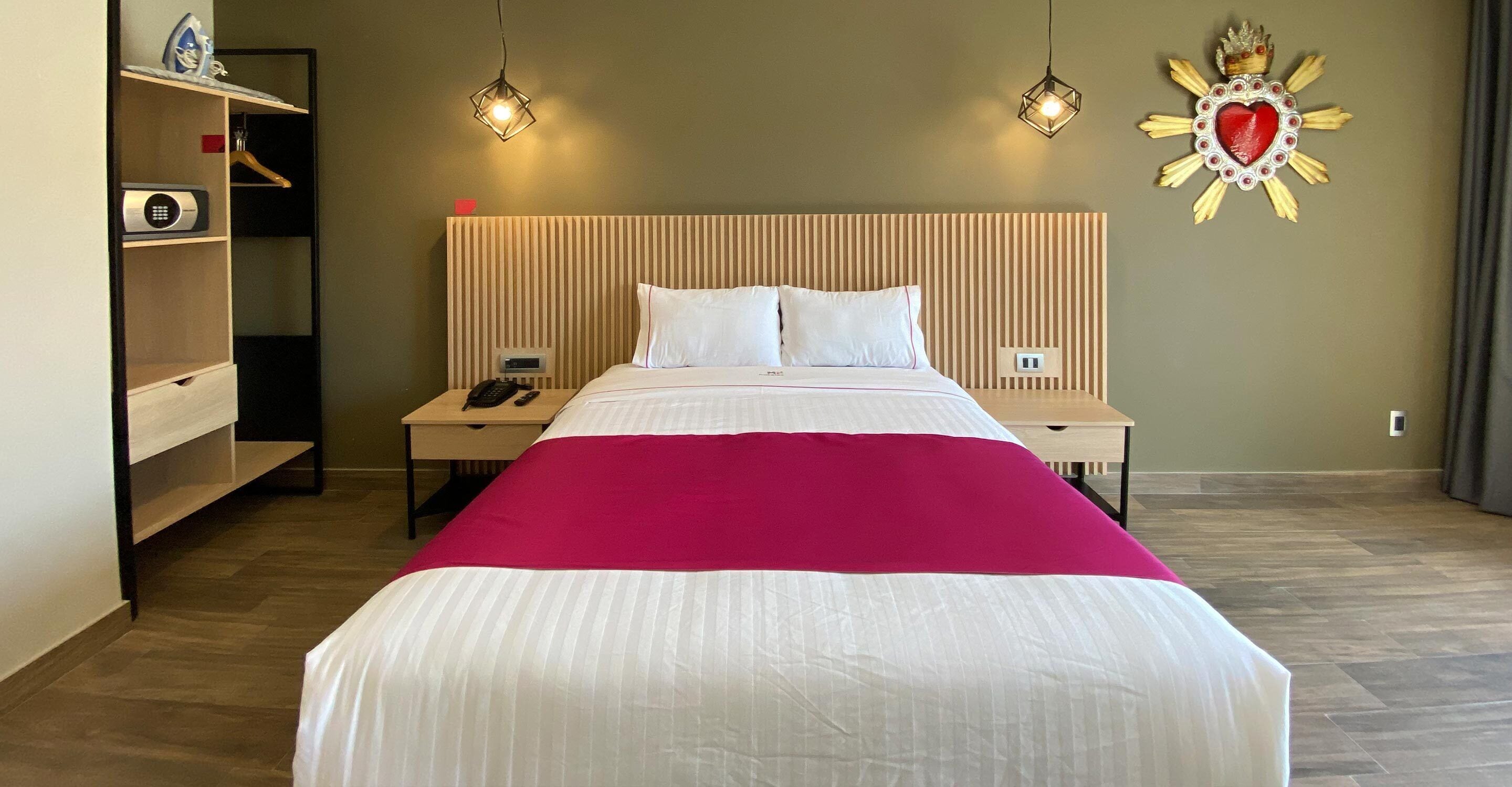 Una habitación de hotel con cama, mesitas de noche, armario y un adorno en la pared.