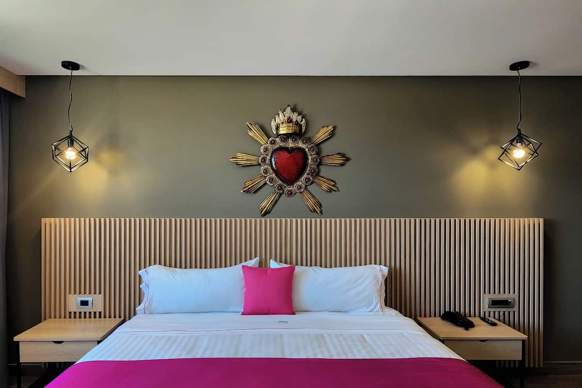 Une chambre d’hôtel avec un grand lit, deux tables de chevet, un élément décoratif fixé au mur et deux luminaires suspendus.