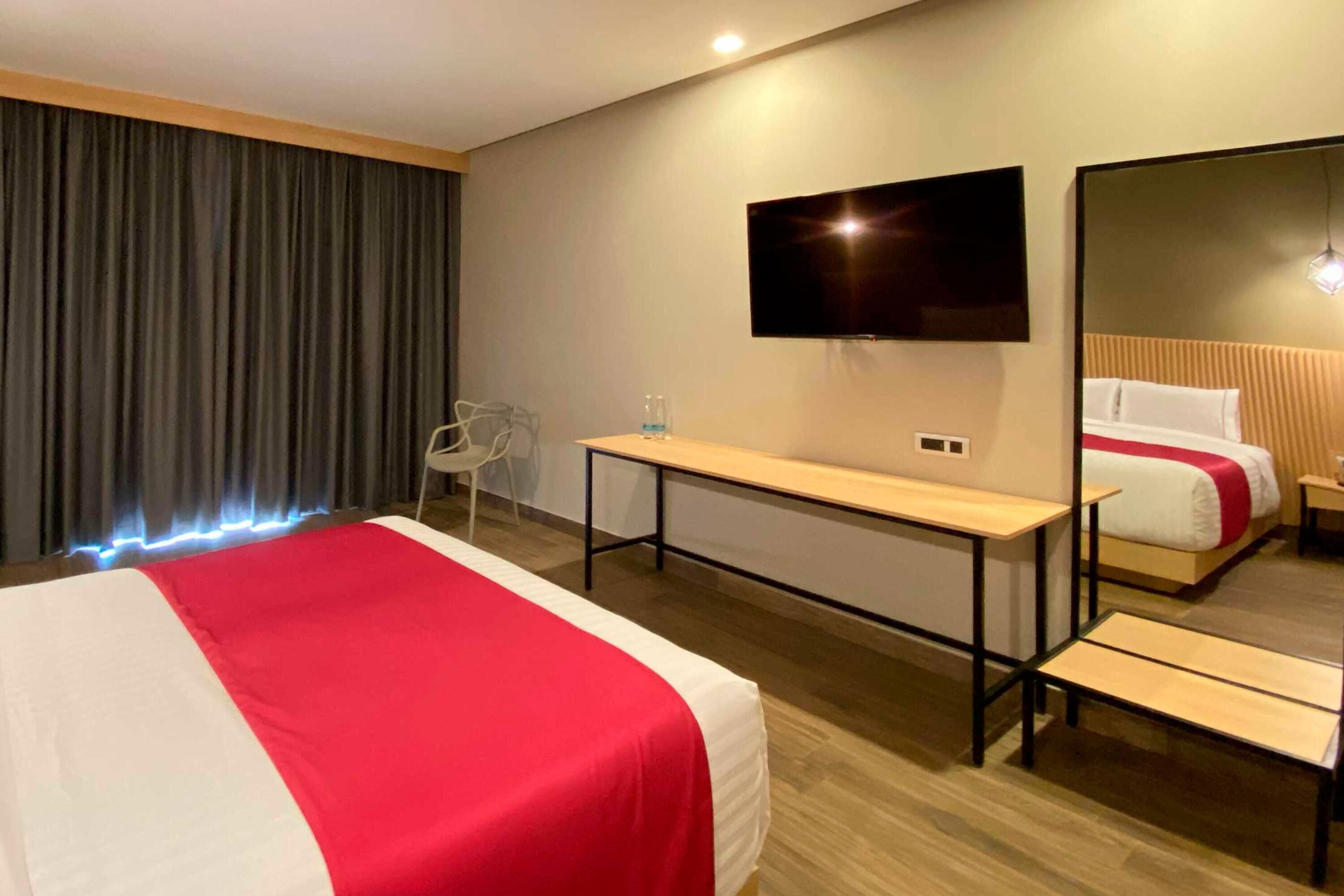 A hotel room with a bed, a TV, a desk, and a chair.