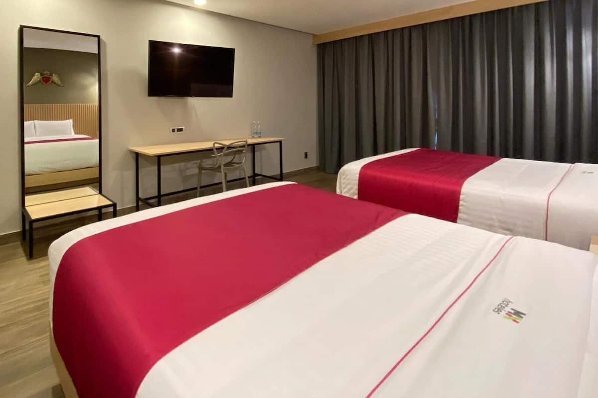Une chambre d’hôtel avec deux lits, un bureau, une chaise, un téléviseur à écran plat et un miroir.