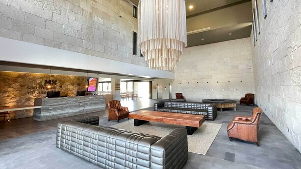 A spacious lobby with a stone wall, leather seating, a reception desk, and a large hanging light fixture. - Hotel MX más San Miguel de Allende (San Miguel de Allende)