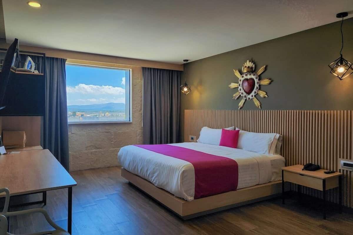 Une chambre d’hôtel équipée d’un lit, d’un bureau, d’une chaise, d’une table de chevet et offrant une vue sur l’extérieur.