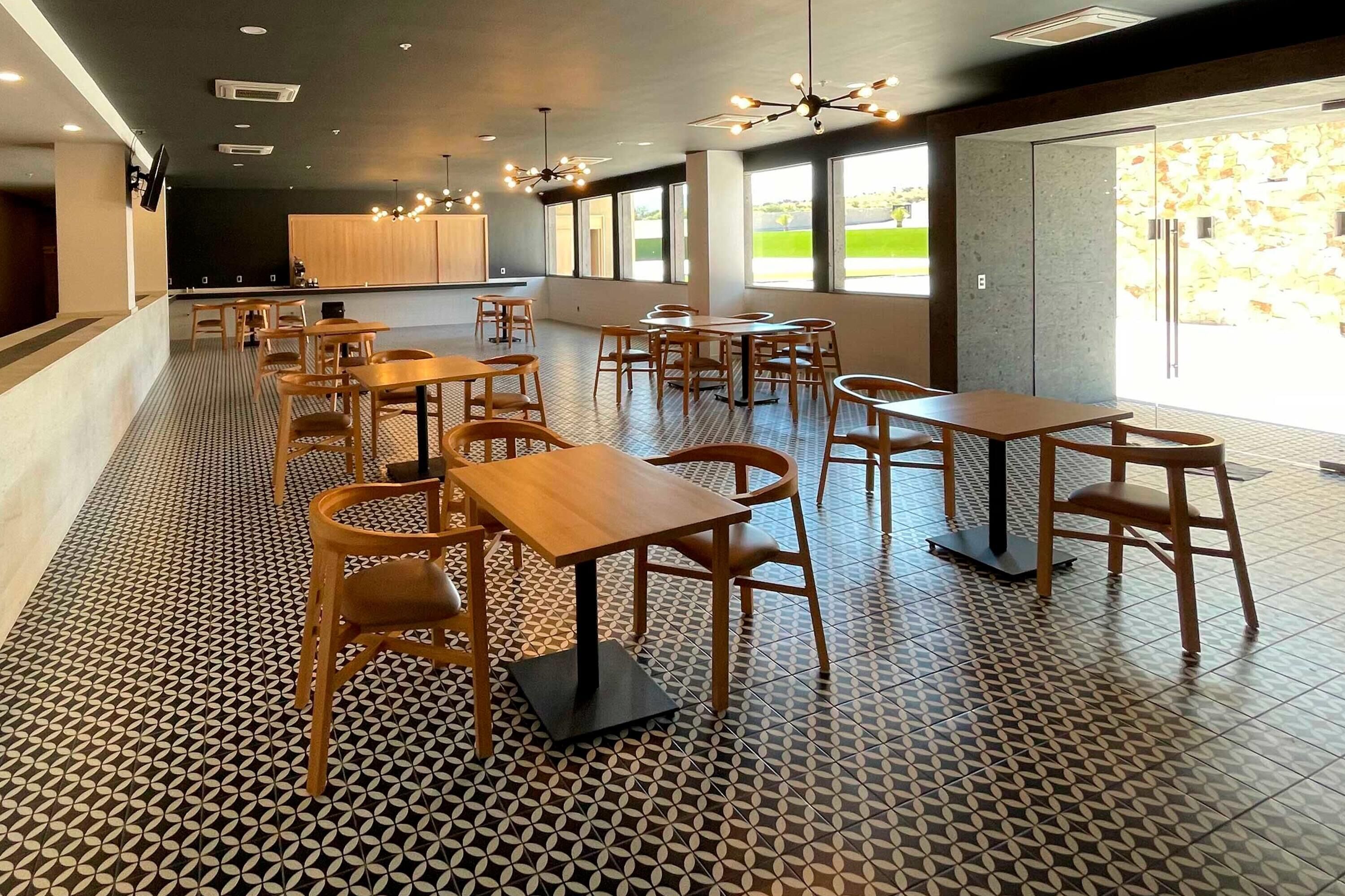 A modern dining area with wooden tables and chairs, a patterned floor, and large windows providing natural light.