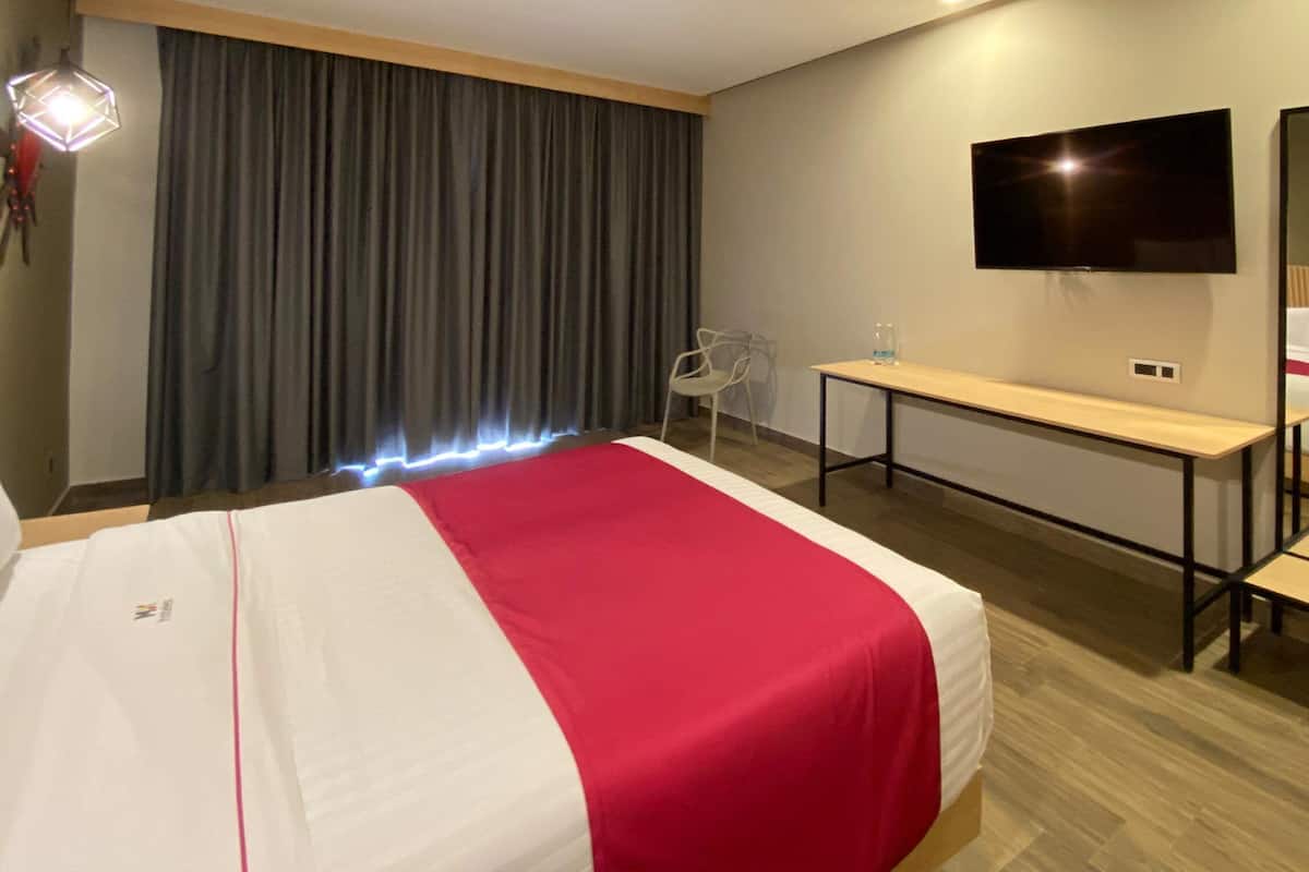Une chambre d’hôtel avec un lit, une télévision, un bureau et un miroir.