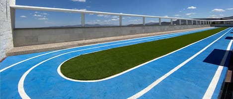 A running track with blue and white markings, a concrete wall, and a clear sky.