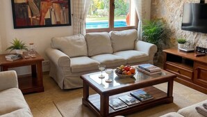 A cozy living room with a sofa, a coffee table with books and a fruit bowl, a painting on the wall, and a TV on a wooden cabinet.