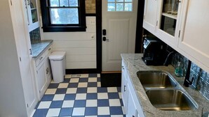 A compact kitchen with a checkered floor, white cabinets, a window, and a door.