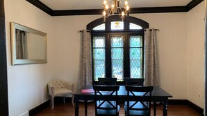A dining area with a table and chairs, a chandelier, a window with curtains, and a mirror on the wall.