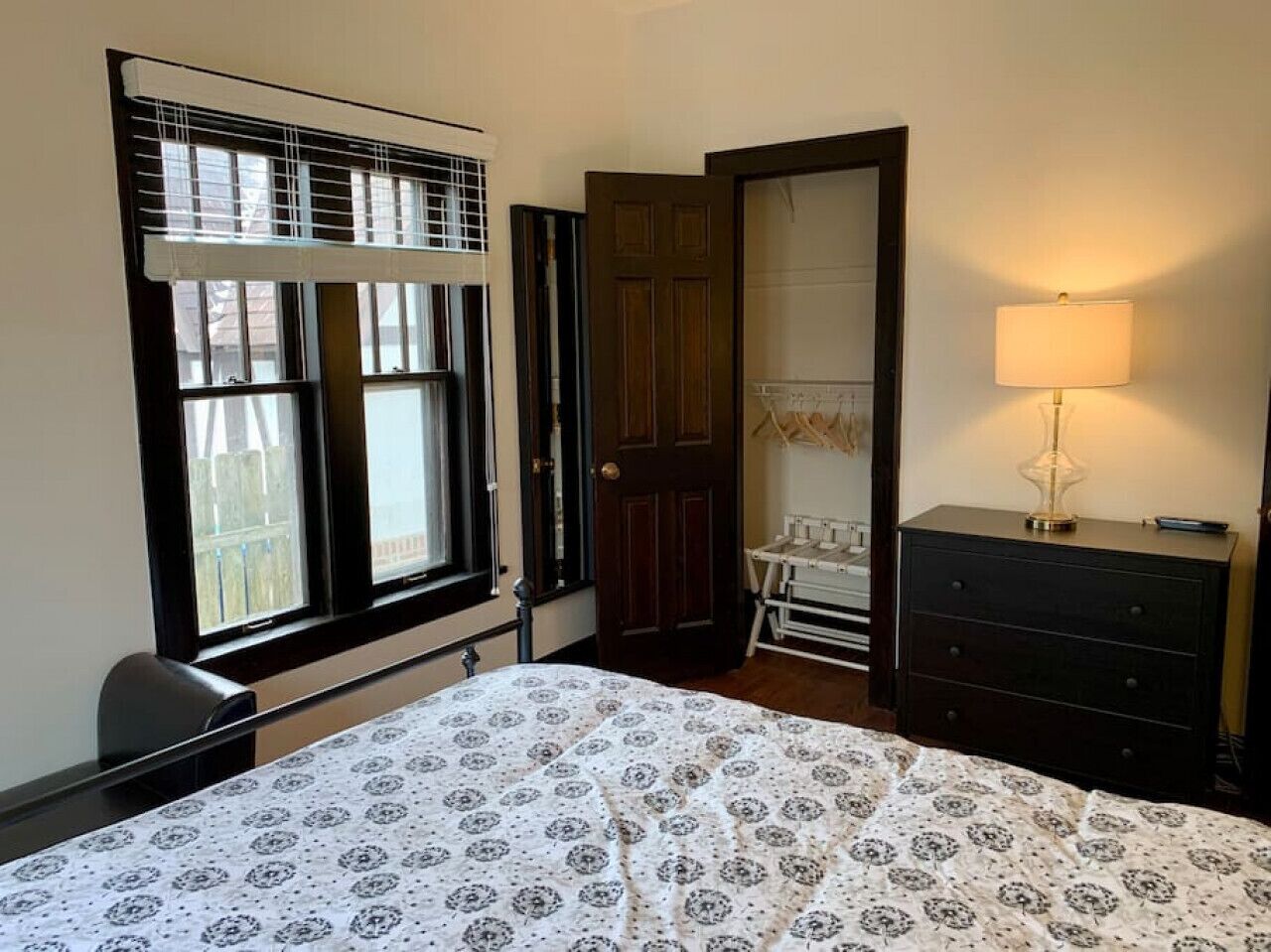 Un dormitorio con cama, cómoda, lámpara, ventana con persianas y puerta.
