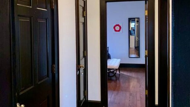 A hallway with wooden flooring, dark doors, and a light fixture on the ceiling.