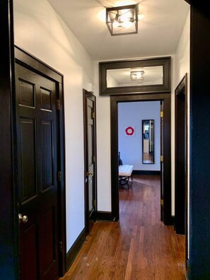 A hallway with wooden flooring, dark doors, and a light fixture on the ceiling. - Tudor house stay-In Town Location! (St. Charles)