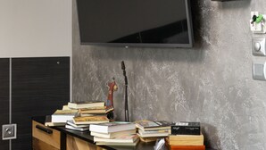 Un salon moderne avec un téléviseur à écran plat fixé au mur, une console en bois et noir ornée de livres et d’une guitare, et un mur gris à texture.
