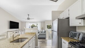 A modern kitchen with granite countertops, stainless steel appliances, and a flat-screen TV.
