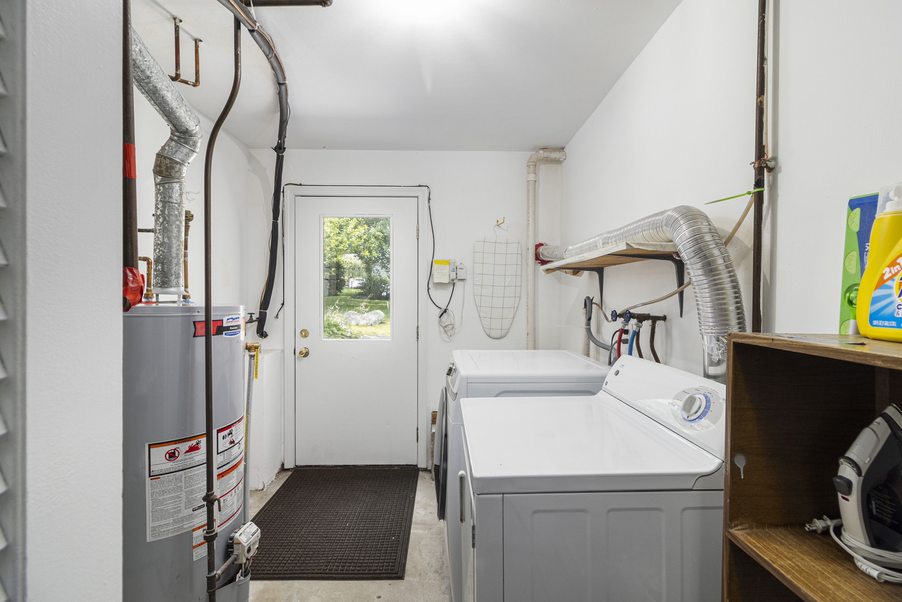A laundry room with a water heater, washing machines, and a vent system.