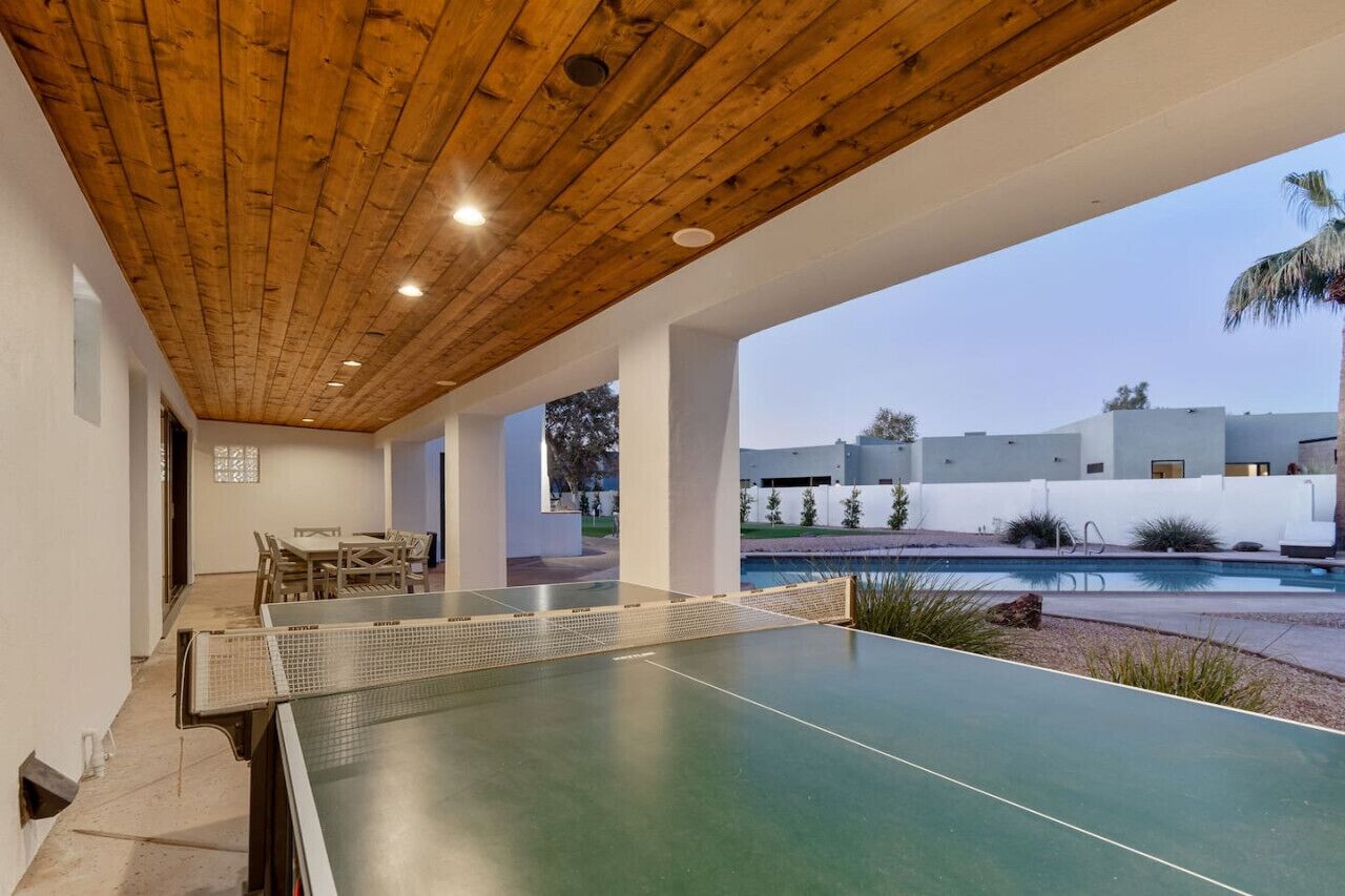 A ping pong table in a covered outdoor area with a pool in the background.