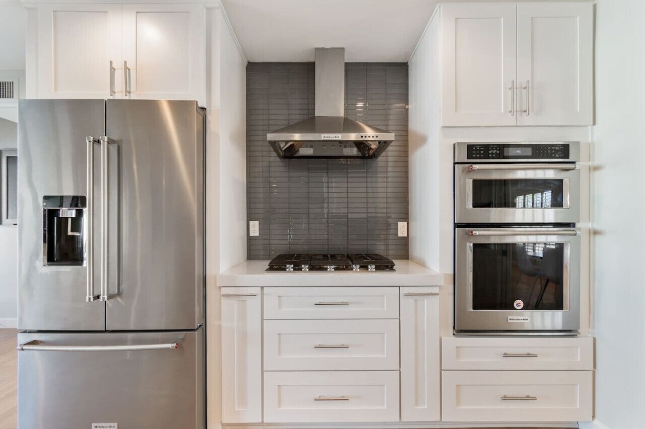 Een moderne keuken met roestvrijstalen apparatuur, witte kasten en een betegelde achterwand.