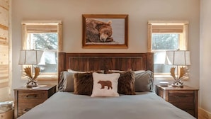Une chambre à coucher avec un grand lit, deux tables de chevet, une tête de lit et un coussin à motifs d’ours.