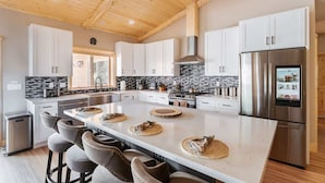 Une cuisine moderne avec des armoires blanches, un grand îlot central, des appareils électroménagers en acier inoxydable et un plafond en bois.