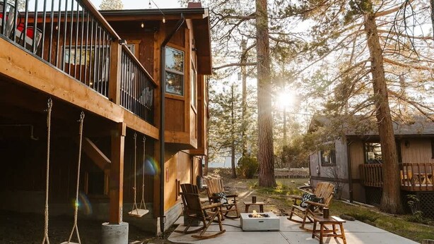 Une cabane en bois dotée d’un balcon, d’un espace salon extérieur et d’un foyer.
