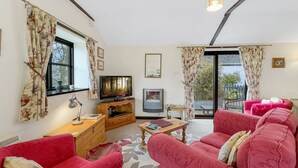 Ein Wohnzimmer mit Fernseher, einem kleinen Tisch, zwei roten Sofas und einem Balkon mit Blick.