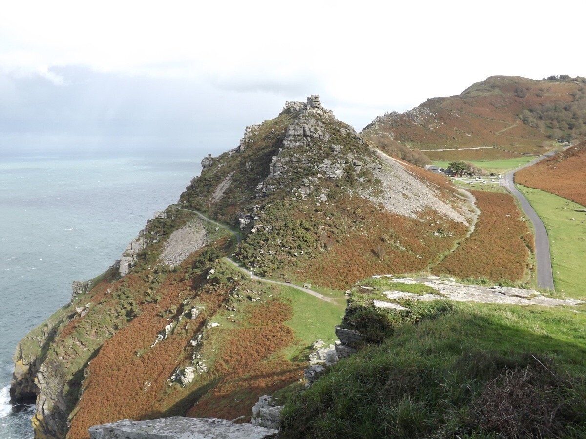 A coastal landscape with a prominent rocky outcrop and a winding road.