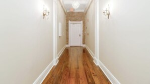A hallway with a wooden floor, white walls, and a brick accent wall. - Historic downtown apartment with a view (Crowley)