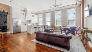 A spacious living area with a dark brown sofa, wooden flooring, white cabinetry, and a dining area with purple chairs. - Historic downtown apartment with a view (Crowley)
