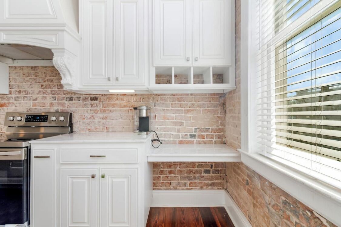 A kitchen with white cabinetry, a brick backsplash, a built-in oven, and a window with blinds.