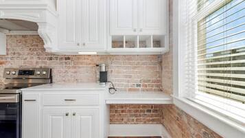 A kitchen with white cabinetry, a brick backsplash, a built-in oven, and a window with blinds.