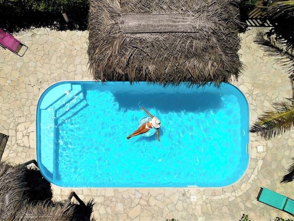 Relax by the pool surrounded by lush palm trees and a thatched lounge area.