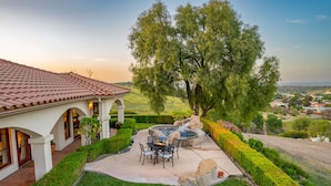 A patio with a hot tub, a dining table, and chairs, surrounded by well-manicured hedges and a large tree. - Luxe Ranch with Hot Tub, Gourmet Kitchen and Fabulous Downtown Views. (Paso Robles)