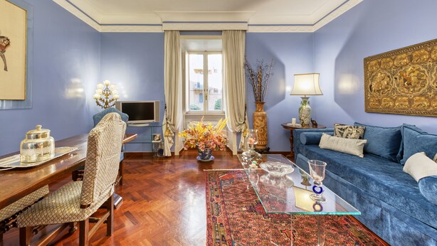 Ein Wohnzimmer mit blauem Sofa, einem Holzesstisch, einer Chandelier und einem großen Gemälde an der Wand.