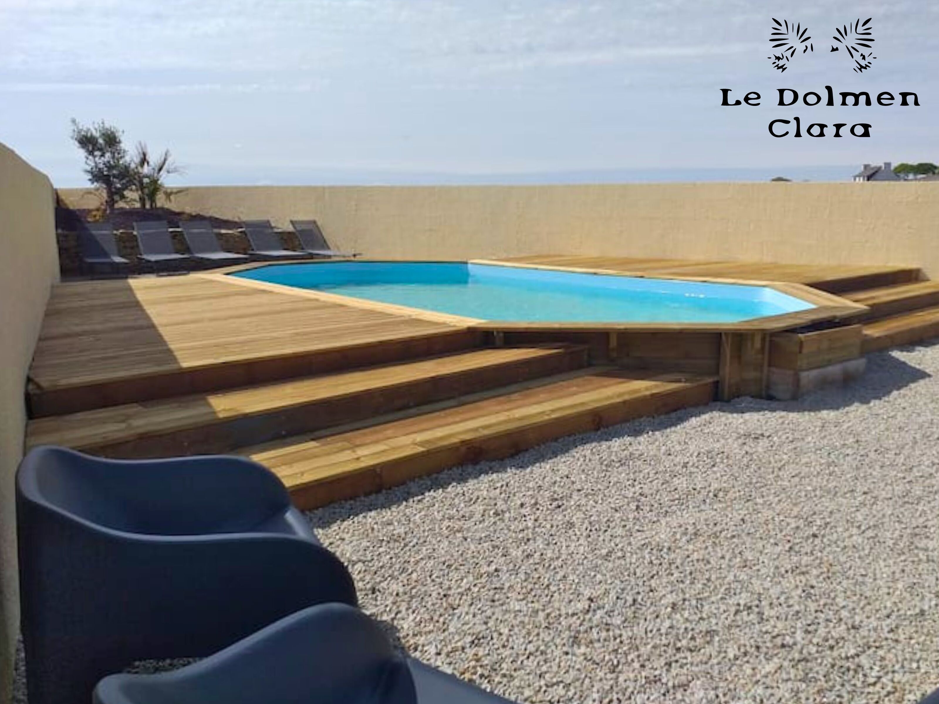 A swimming pool with wooden steps leading to a lounge area with sun loungers.
