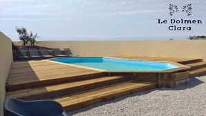 Ein Swimmingpool mit Holzstufen, die zu einem Liegebereich mit Sonnenliegen führen.