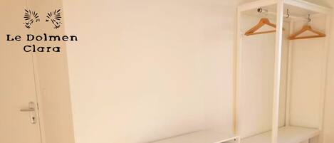 A white wardrobe with a mirror, a small stool, and a white shelf unit.