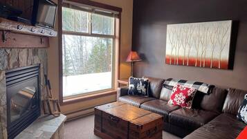 A cozy living room with a stone fireplace, leather sofa, and a large window.
