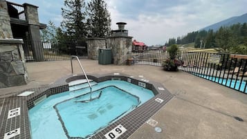 A hot tub with a stone exterior and a poolside area with a fence and a mountain view.