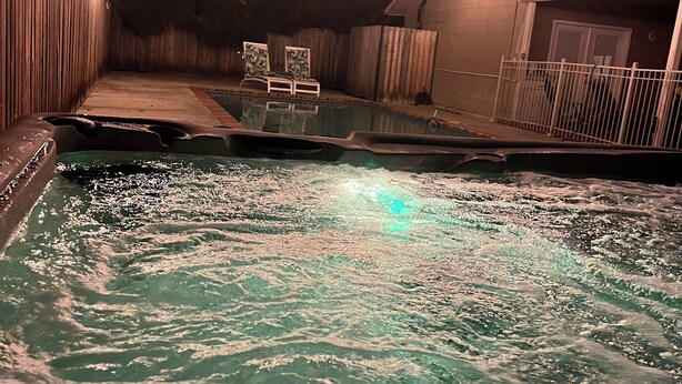 A hot tub with water jets, surrounded by a wooden deck and a white fence.