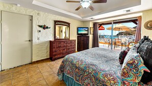 Un dormitorio con cama, cómoda, televisor y vista a la playa a través de un ventanal corredero.