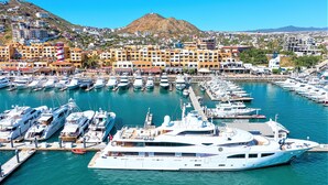 Un puerto deportivo con varios yates amarrados, rodeado de edificios y una colina al fondo.