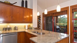 Une cuisine dotée de meubles en bois, de plans de travail en granit, d’appareils électroménagers en acier inoxydable et de luminaires suspendus.