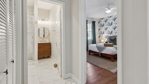 A hallway leading to a bathroom with a marble floor and a wooden vanity.