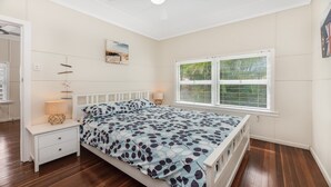Une chambre à coucher comprenant un lit, des tables de chevet, une fenêtre avec des stores et un tableau accroché au mur.