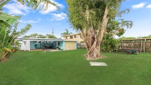 Patio trasero residencial con una casa, un garaje, un árbol y un área cercada.