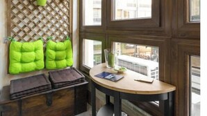 A cozy corner with a wooden bench, a small table, and a window with a view of buildings. - Emerald central luxury mini suite (Thessaloniki)