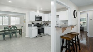 A modern kitchen with white cabinets, a stainless steel oven, and a microwave. There is a dining area with a table and chairs. - Upgraded 3B/2Bth w DinningR on Peaceful Street (Fresno)